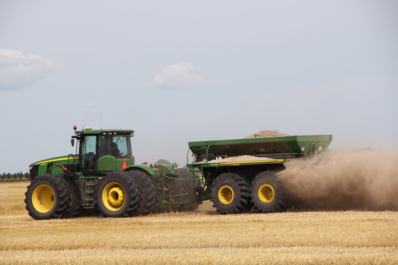 Modern tractor pulling a fertilizer spreader across a harvested field, representing livestock financing, skid steer financing for farms, farmland loans, farm renewable energy financing, and agricultural financing companies that support equipment purchases, land acquisition, livestock expansion, renewable energy improvements, and long-term farm growth.